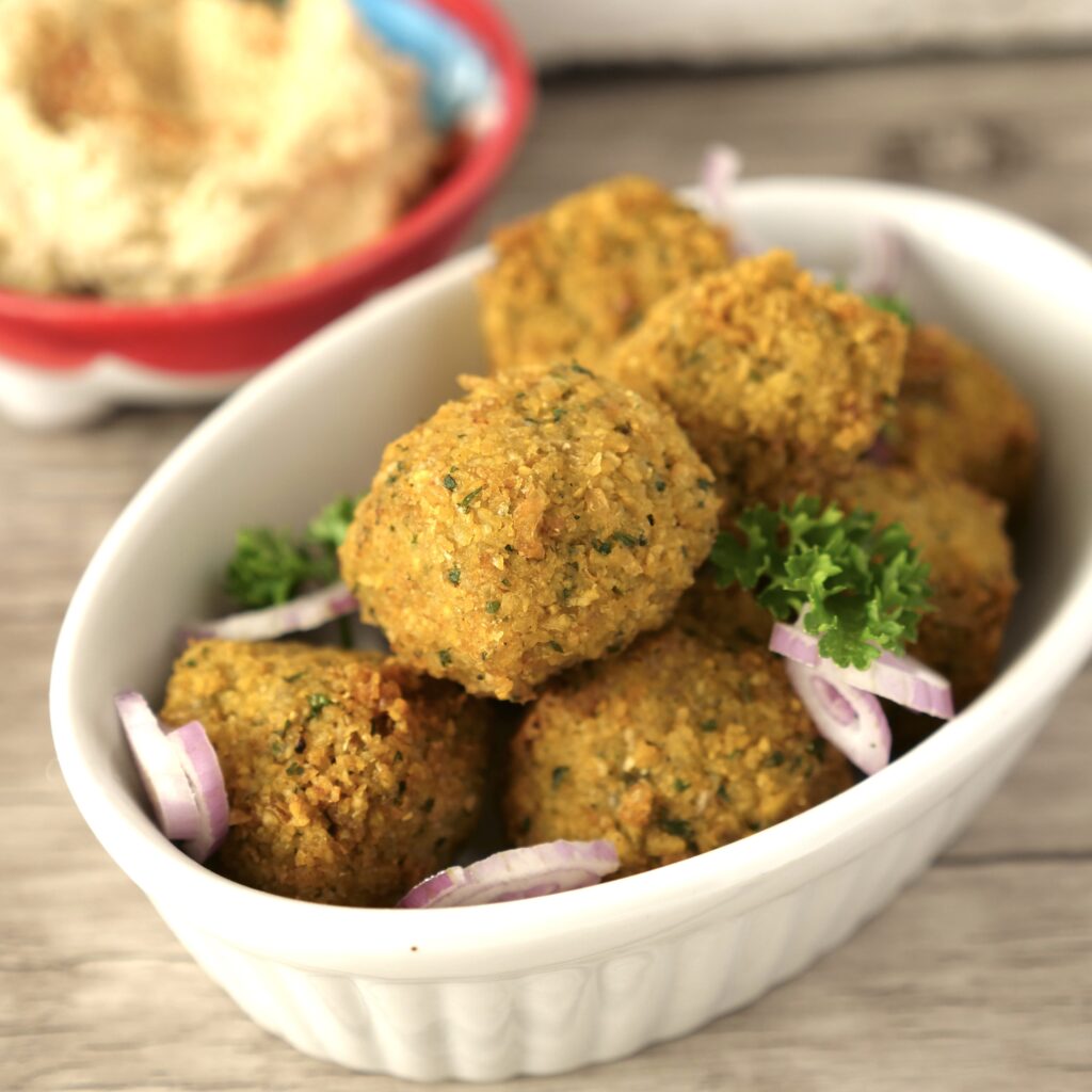 falafel balls in a white bowl with parsley & shallots